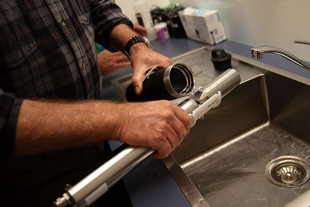 A man pours drinking water into a silver cylindrical shaped spectrometer to test for nitrate contamination.